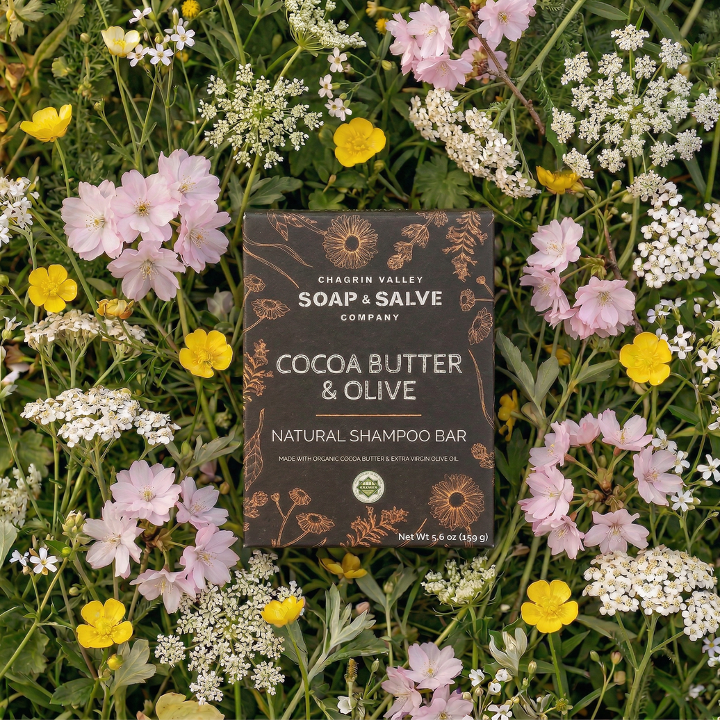 Cocoa Butter & Olive natural shampoo bar packaging surrounded by wildflowers