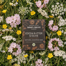Cocoa Butter & Olive natural shampoo bar packaging surrounded by wildflowers