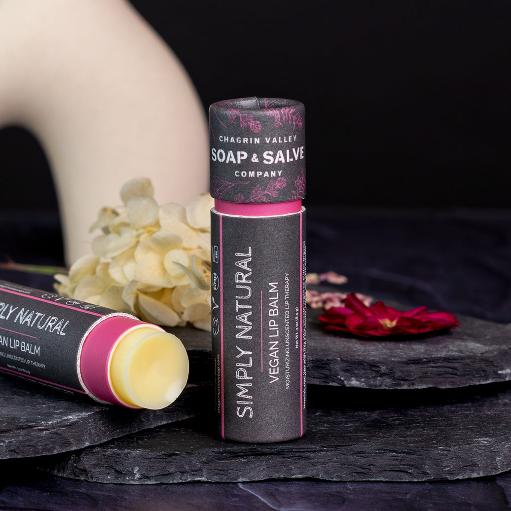 Simply Natural Vegan Lip Balm stick on a dark slate background with flowers, showcasing natural vegan lip balm ingredients.