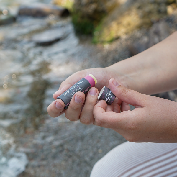 Natural vegan lip balm stick in hands by a stream, showcasing rich moisture and plant-based ingredients.
