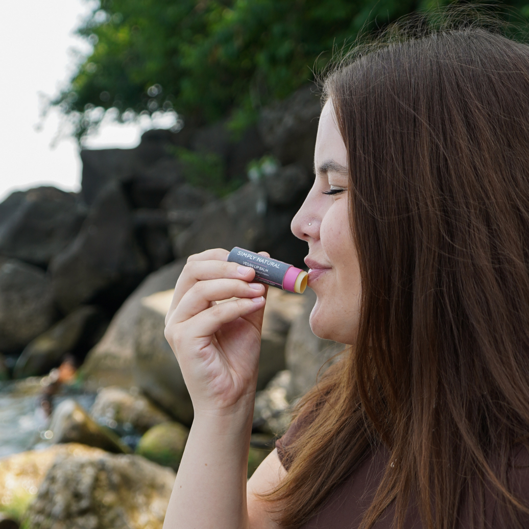 Woman enjoying natural vegan lip balm stick by the beach, showcasing its moisturizing texture.