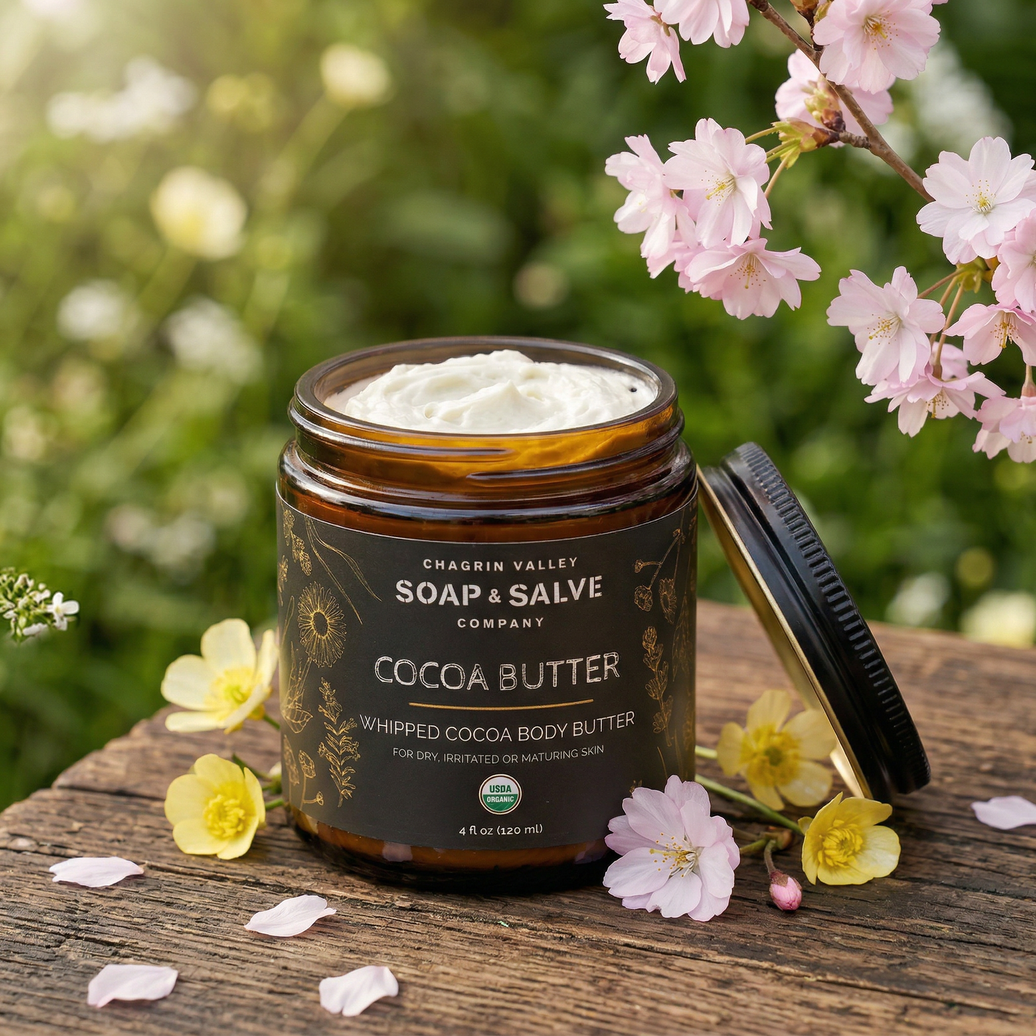 Jar of Chagrin Valley Soap & Salve Company Cocoa Butter Whipped Cocoa Body Butter on a wooden surface with flowers.